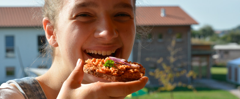 Eine junge Frau beißt in ein Brot welches mit veganem Mett bestrichen ist